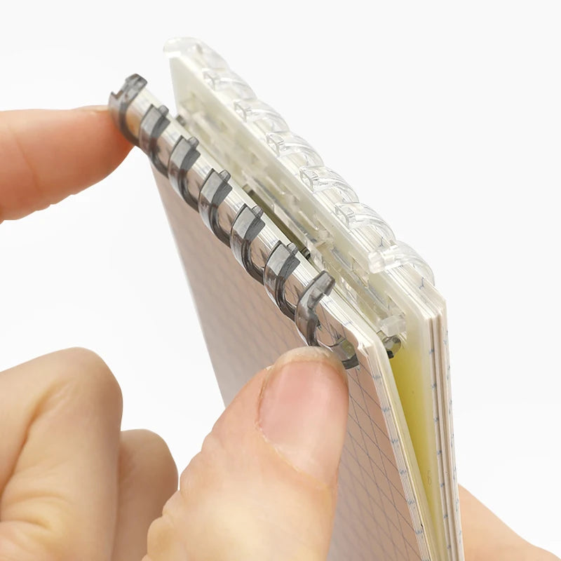 Small spiral-bound notebook held between fingers against a white background