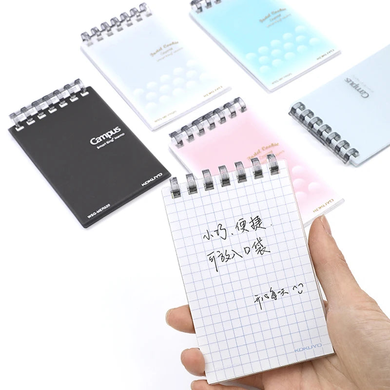 Small notebooks with different designs and a hand holding one with grid paper.
