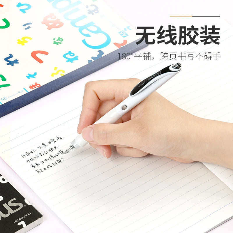 Hand holding a white pen over a notebook with colorful letters in the background