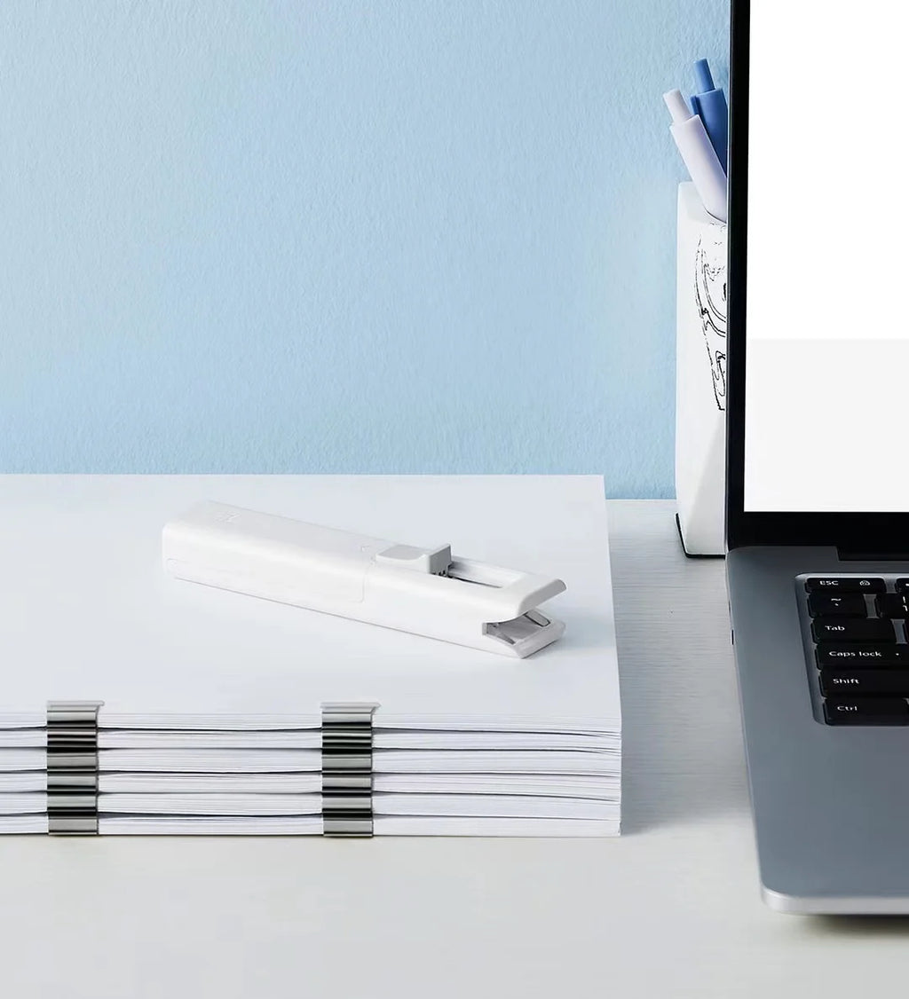 Bentopop paper clips on a stack of papers with a laptop and pen holder on a light blue background