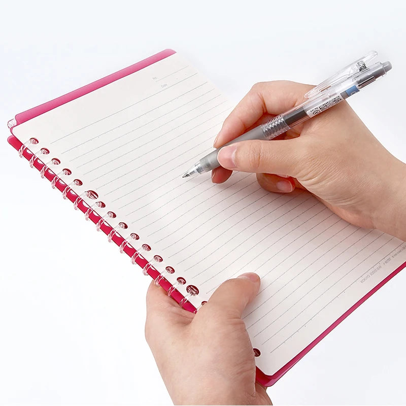 Hand holding a pen over a small notebook with a pink binding on a white background